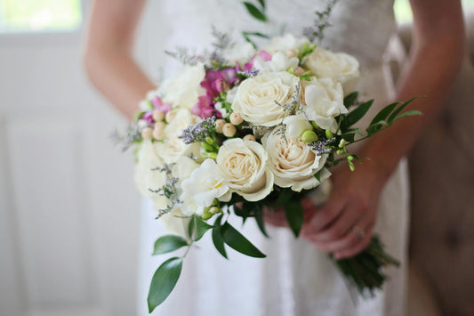 Bride holding a wedding bouquet of white roses, greenery, and delicate accents.