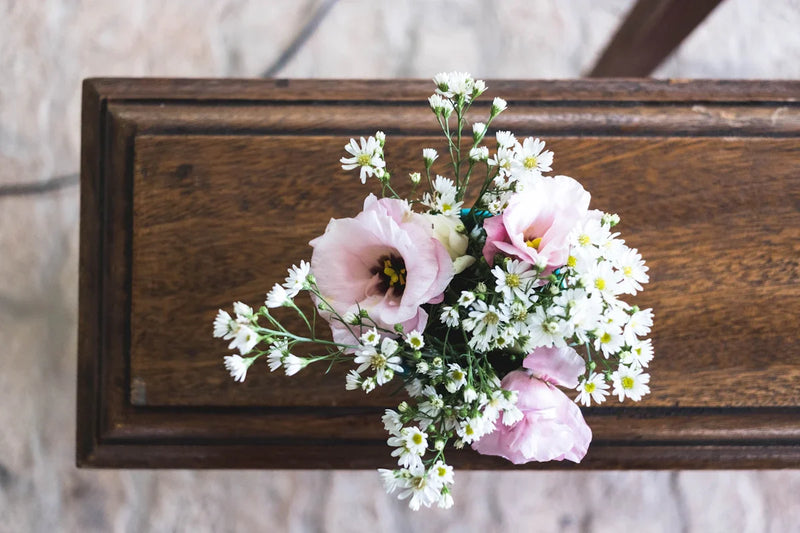 Pink and white funeral flowers resting on a wooden casket