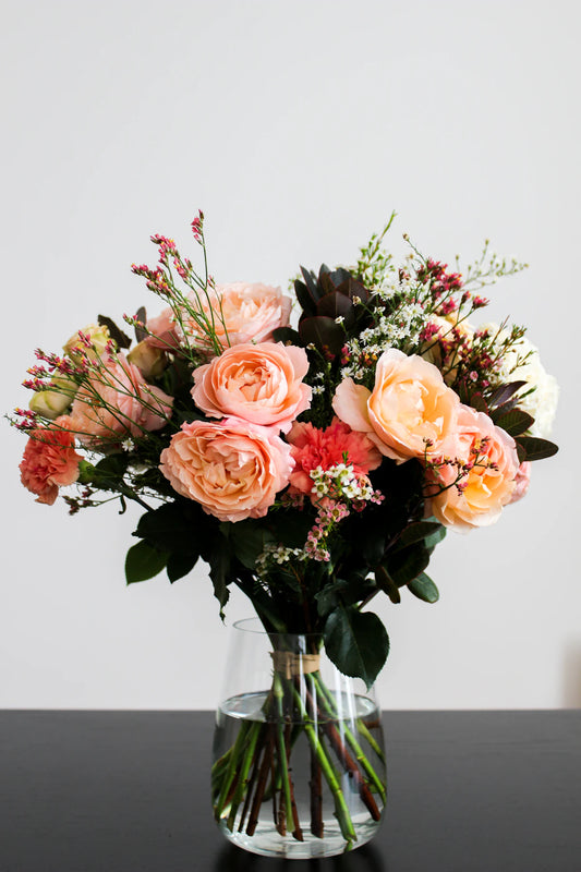 Fresh flower subscription bouquet of peach garden roses and carnations in a glass vase