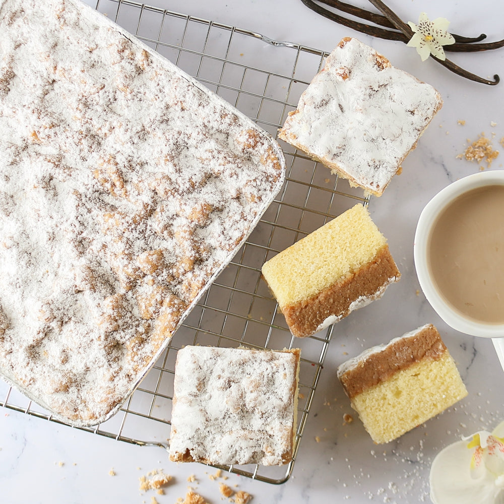 Square slices of cake on a cooling rack with a cup of coffee and vanilla beans.