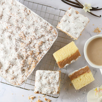 Square slices of cake on a cooling rack with a cup of coffee and vanilla beans.