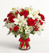 Fields of Europe Christmas Bouquet of red roses and white lilies with a red ribbon in a clear vase on a light gray background