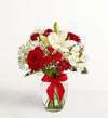 Fields of Europe Christmas Bouquet of red roses and white lilies in a clear vase with a red ribbon on a white background