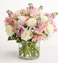 Bouquet of pink, white, and purple flowers in a clear glass vase on a white background