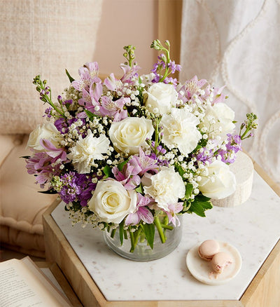 White roses with pink alstroemeria, purple stock, white carnations and baby's breath arranged in a clear glass vase. White roses with pink alstroemeria, purple stock, white carnations and baby's breath arranged in a clear glass vase.