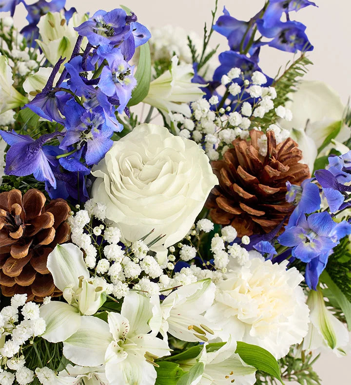 Bouquet of flowers with white roses, blue delphinium, and pinecones.