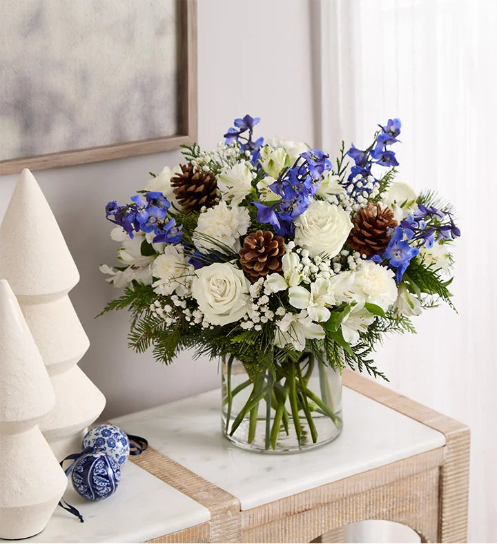 Winter Wishes Bouquet of flowers with blue and white flowers in a vase on a table.