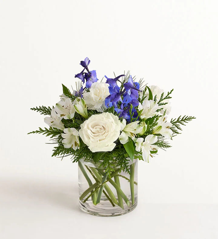 Winter Wishes Bouquet of white and blue flowers in a clear vase on a light background