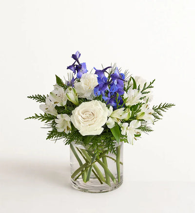 Winter Wishes Bouquet of white and blue flowers in a clear vase on a light background Winter Wishes Bouquet of white and blue flowers in a clear vase on a light background