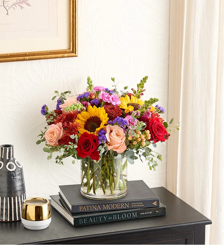 Colorful bouquet of flowers in a clear vase on a stack of books with a decorative background.