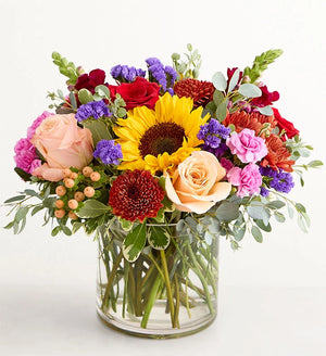 Harvest Melody Bouquet Colorful flower bouquet with sunflowers, roses, and other flowers in a clear vase on a white background