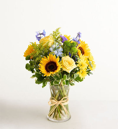 Bouquet of sunflowers and yellow roses in a clear vase on a white background Bouquet of sunflowers and yellow roses in a clear vase on a white background