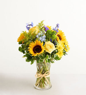 Bouquet of sunflowers and yellow roses in a clear vase on a white background