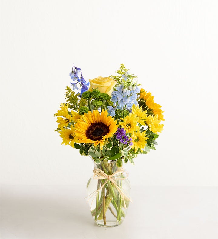 Bouquet of sunflowers, roses, and other flowers in a glass vase on a white background