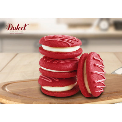 Red cookies with white filling on a wooden board, featuring the Dulced brand.