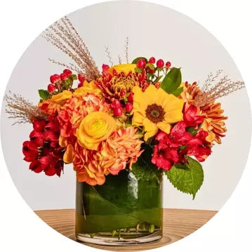 Colorful fall flower arrangement in a glass vase on a light background