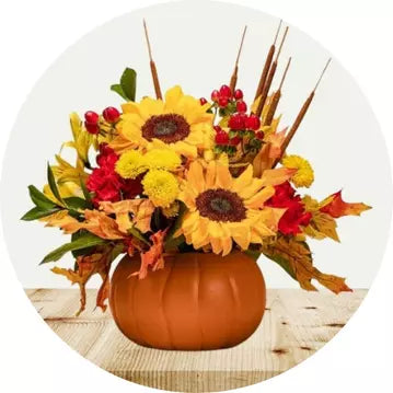 Autumn-themed floral arrangement in a pumpkin vase on a wooden surface.