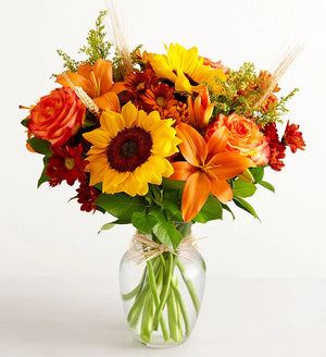 Bouquet of flowers with sunflowers, roses, and lilies in a clear vase on a white background