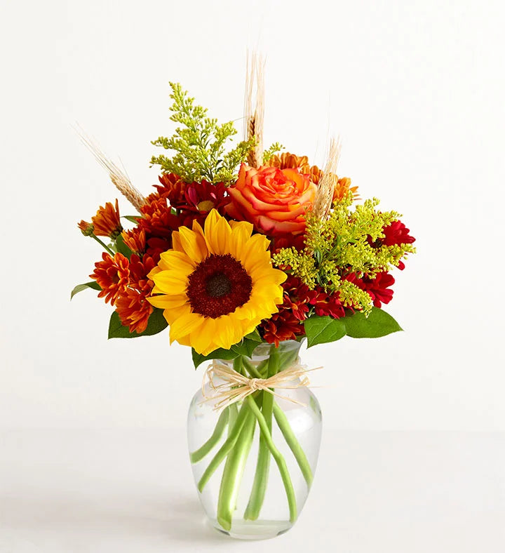 Bouquet of flowers with sunflowers, roses, and greenery in a clear vase on a white background
