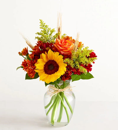Bouquet of flowers with sunflowers, roses, and greenery in a clear vase on a white background Bouquet of flowers with sunflowers, roses, and greenery in a clear vase on a white background