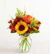 Bouquet of flowers with sunflowers, roses, and greenery in a clear vase on a white background