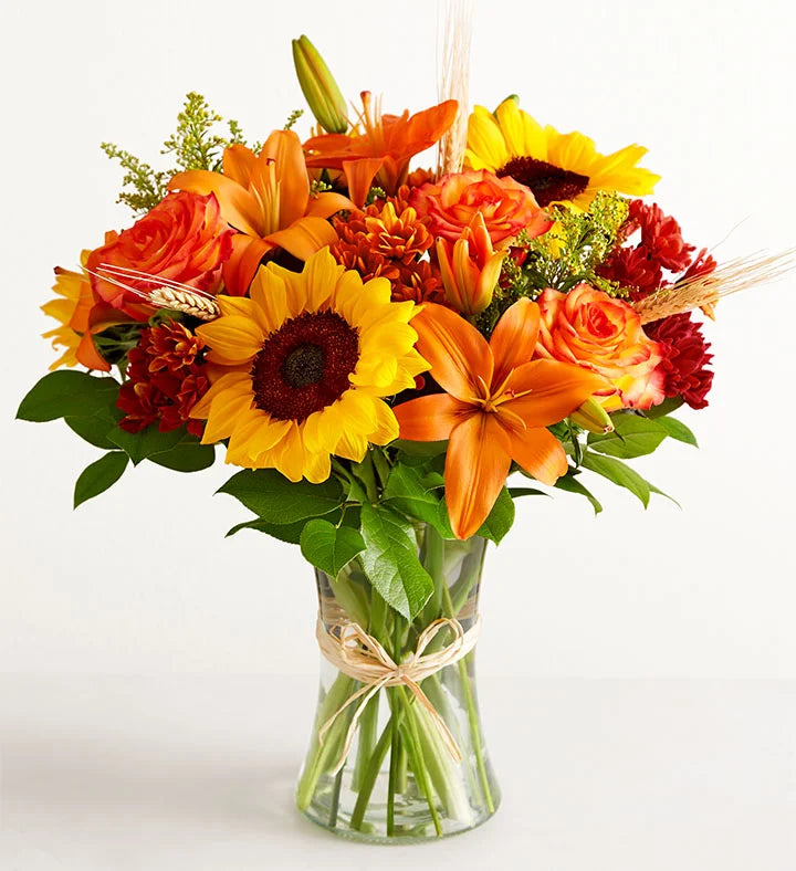 Bouquet of flowers with sunflowers, lilies, and mums in a clear vase on a white background