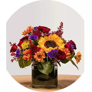 Friendsgiving Bouquet of colorful flowers in a glass vase on a wooden surface with a white background