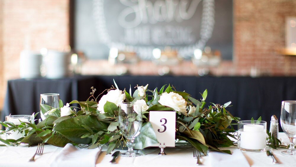 a wedding centerpieces in side a wedding venue with text that reads View which venues James Cress Florist is the in-house Florist.