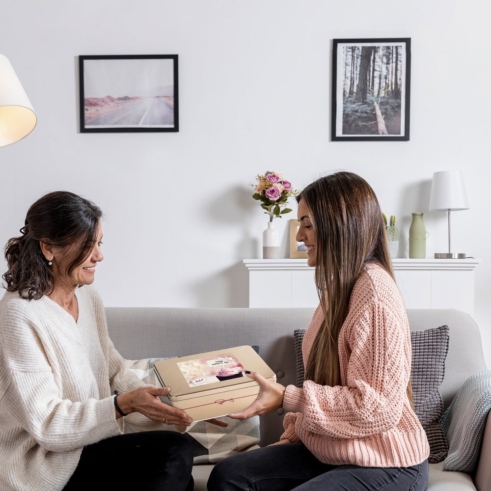 Two women sitting on a couch in a living room, one giving a gift to the other.