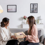 Two women sitting on a couch in a living room, one giving a gift to the other.
