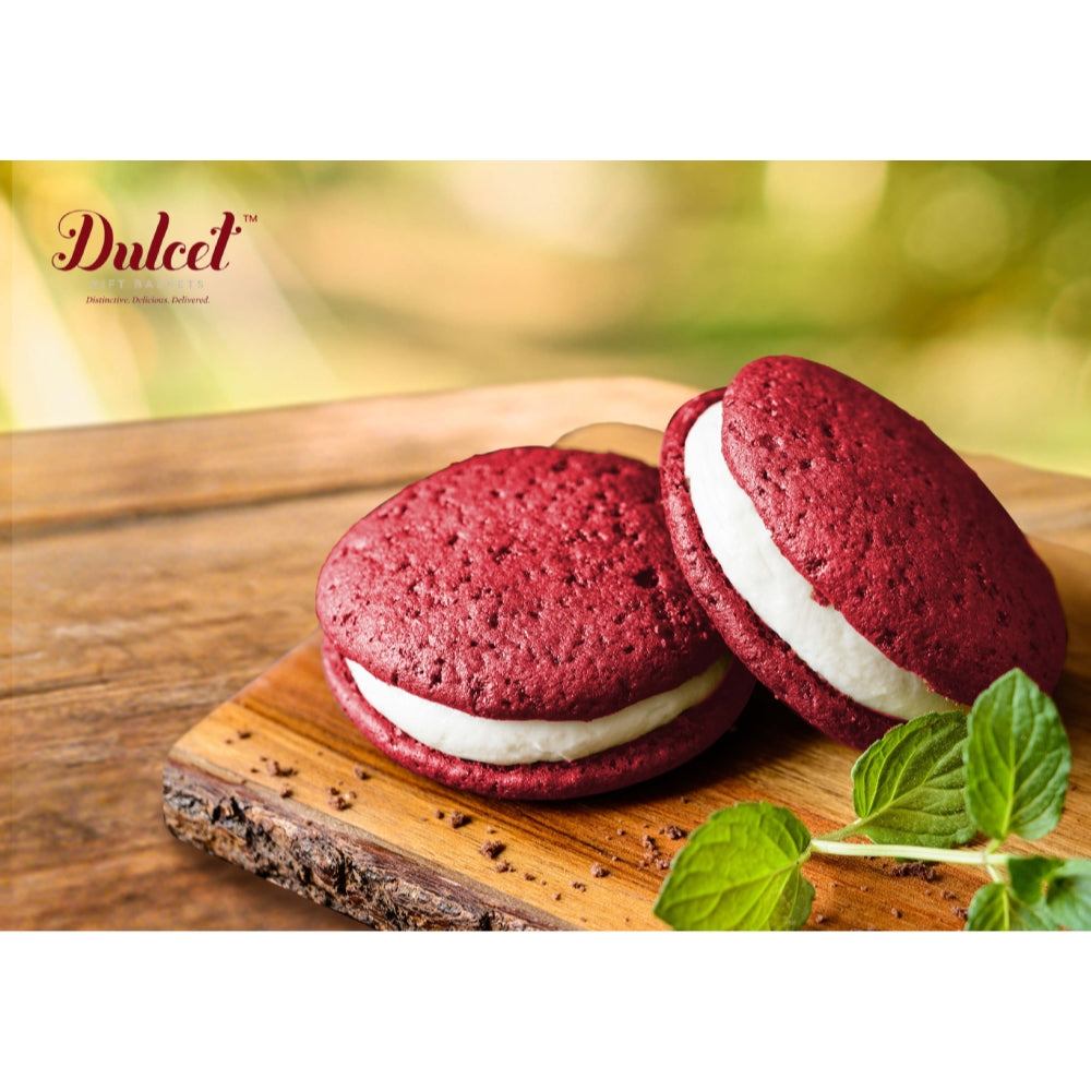 Red velvet whoopie pies with white filling on a wooden board, brand 'Dulced' visible.