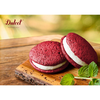 Red velvet whoopie pies with white filling on a wooden board, brand 'Dulced' visible.