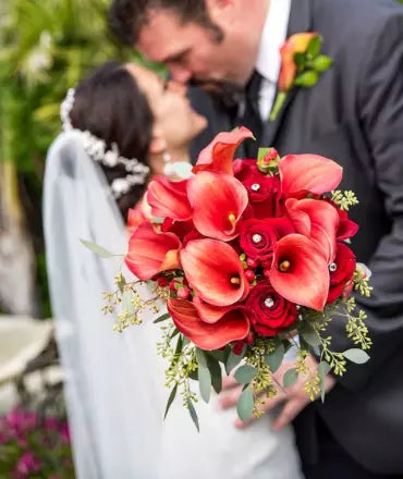 A bride and groom with a red calla lily bouquet by James Cress Florist