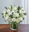 Medium Elegant all-white sympathy floral arrangement in a clear glass cylinder vase, featuring white roses, snapdragons, alstroemeria, carnations, and monte casino, accented with lush greenery and a Ti leaf ribbon. Perfect for memorials or as a thoughtful gift.