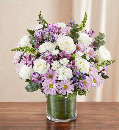 Medium Sympathy floral arrangement in lavender and white, featuring lavender roses, alstroemeria, carnations, white snapdragons, and daisy poms in a clear glass cylinder vase lined with a Ti leaf ribbon. A touching tribute for remembrance, perfect for home or service. Medium Sympathy floral arrangement in lavender and white, featuring lavender roses, alstroemeria, carnations, white snapdragons, and daisy poms in a clear glass cylinder vase lined with a Ti leaf ribbon. A touching tribute for remembrance, perfect for home or service.