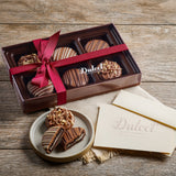 Chocolate assortment in a box with a red ribbon on a wooden surface, featuring the brand 'Dulce'.