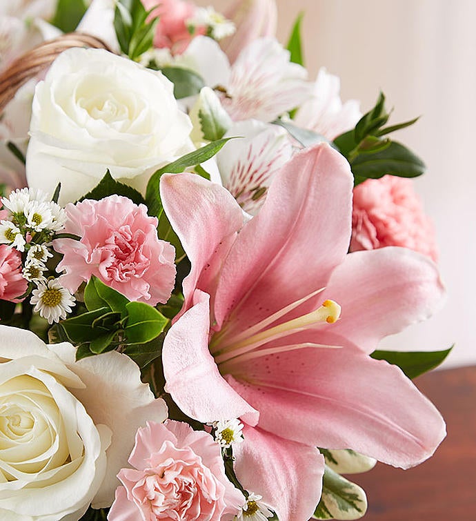 Zoomed in picture of Elegant pink and white floral arrangement in a wicker basket, featuring pink Asiatic lilies, carnations, and mini carnations, complemented by white roses, alstroemeria, monte casino, and lush greenery, ideal for expressing sympathy and care.