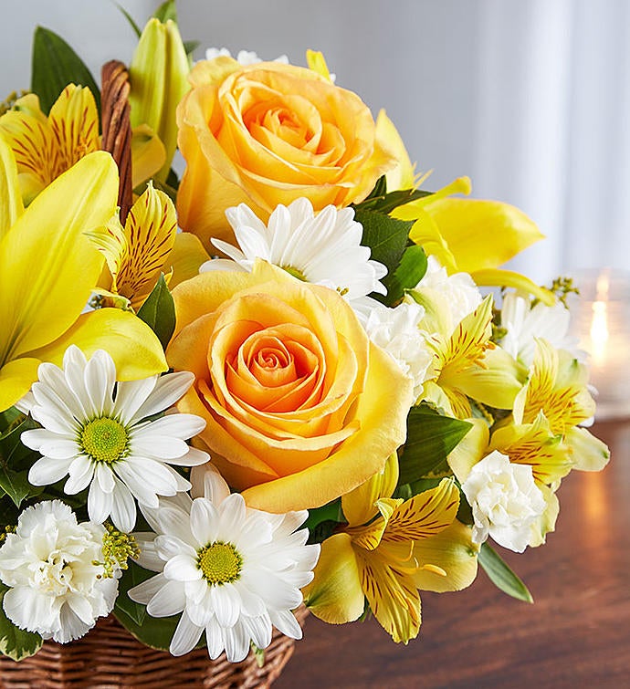 Zoomed in picture of yellow and white floral arrangement in wicker basket featuring yellow roses, Asiatic lilies, alstroemeria, white daisy poms, and mini carnations with lush greenery, perfect for conveying support and blessings.