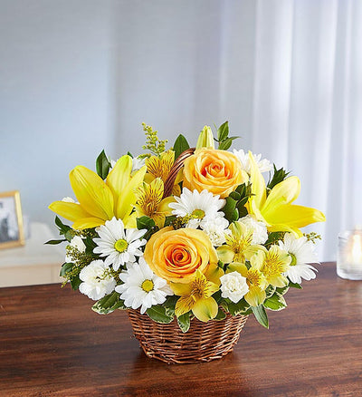 Small yellow and white floral arrangement in wicker basket featuring yellow roses, Asiatic lilies, alstroemeria, white daisy poms, and mini carnations with lush greenery, perfect for conveying support and blessings. Small yellow and white floral arrangement in wicker basket featuring yellow roses, Asiatic lilies, alstroemeria, white daisy poms, and mini carnations with lush greenery, perfect for conveying support and blessings.